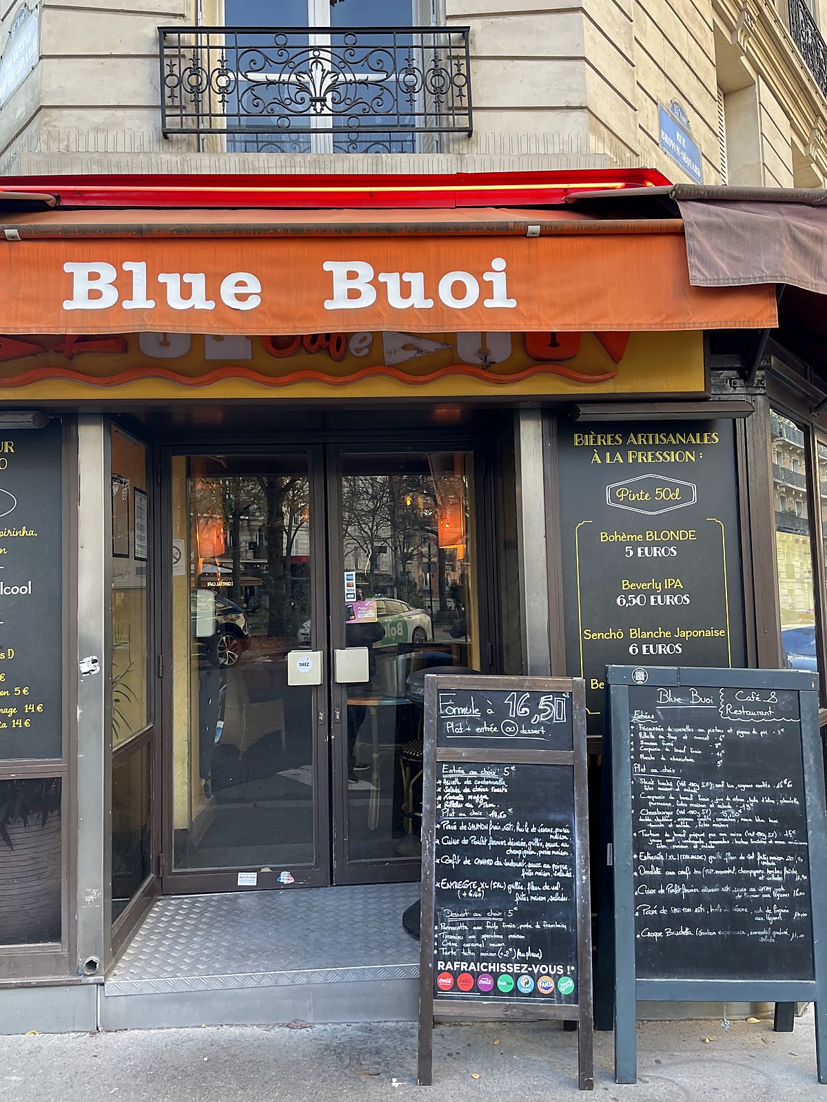 L'entrée du café, store orange et ardoises de menu.