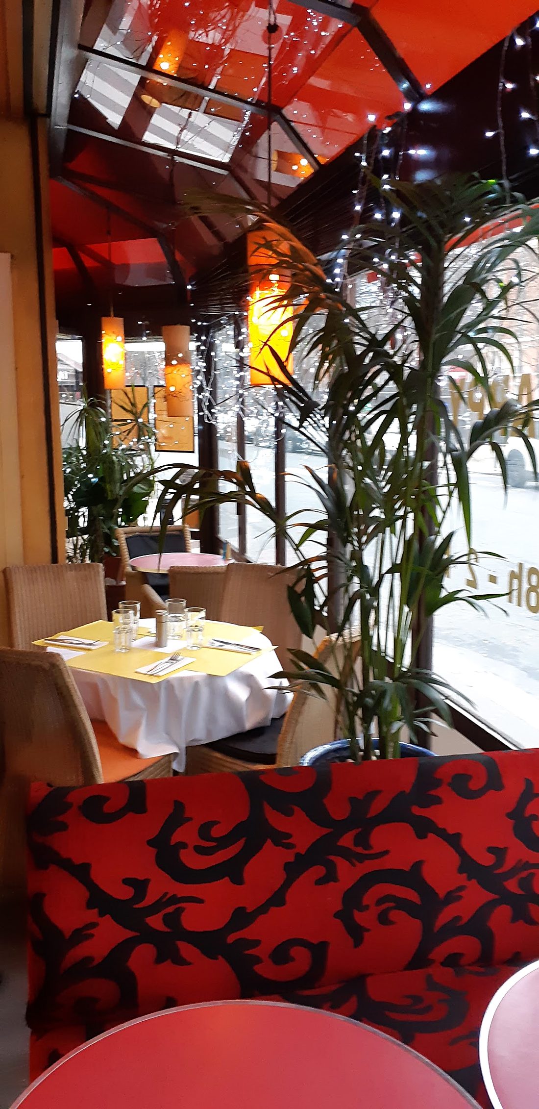 La véranda, banquette et tables dressées parmi les plantes.